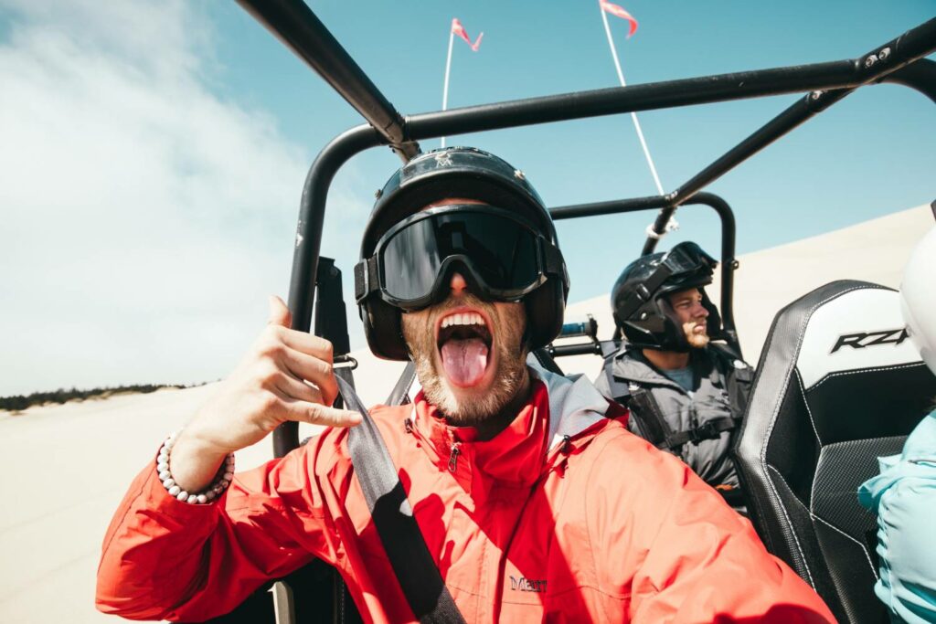 A man on a dune buggy in a desert livestreaming his adventure with his tongue out.