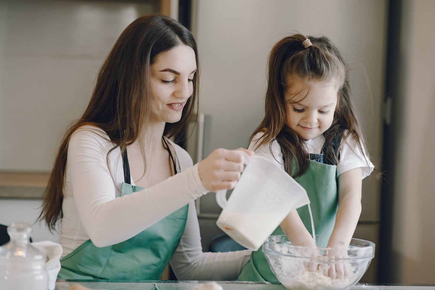 a woman and a child mixing materials in a bowl while wearing aprons, perhaps they are making a science project