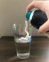 a photo of a person spraying shaving cream into a glass of water for a science project experiment creating a storm in a glass