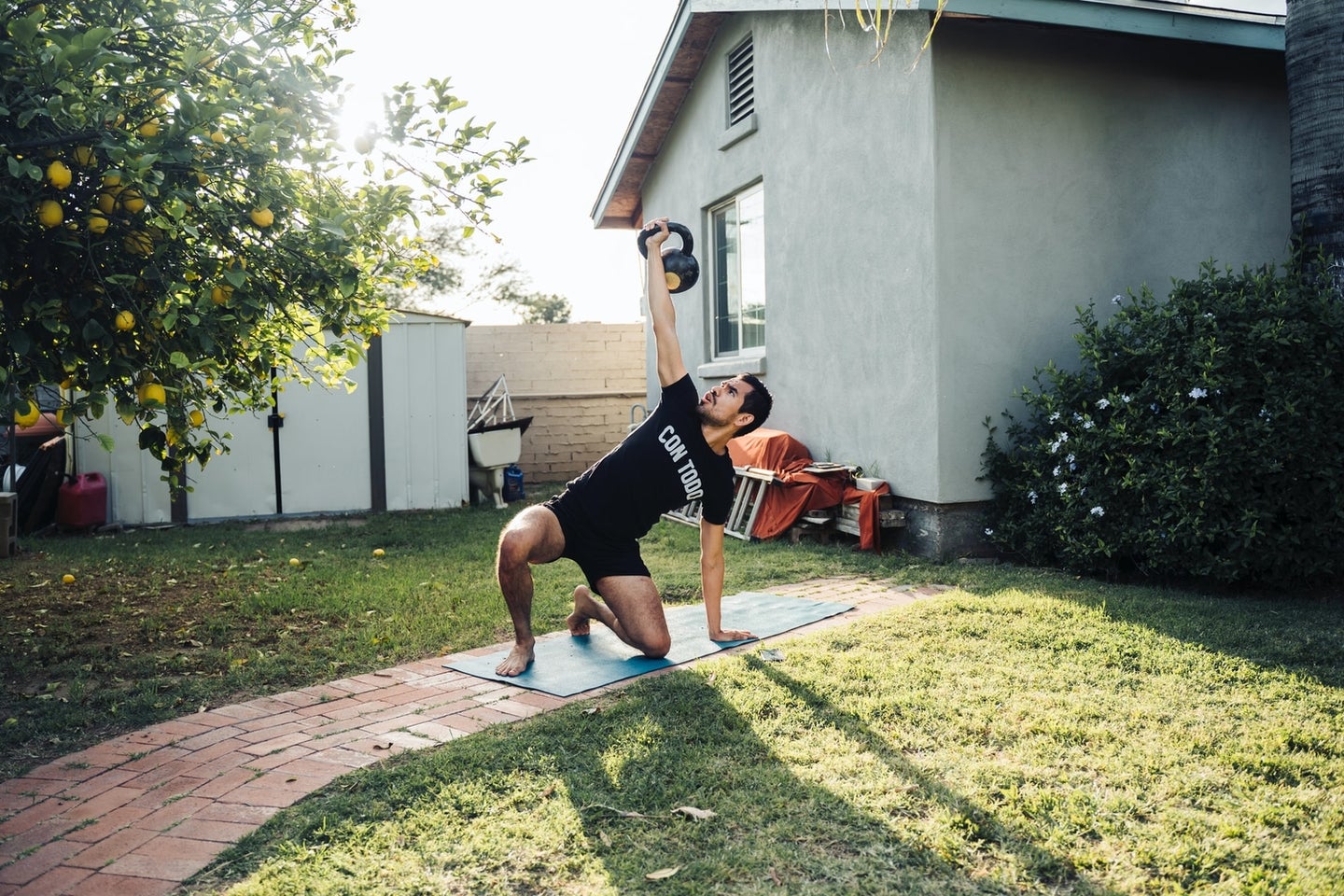 a man in workout clothes lifting a kettlebell on a yoga mat outside at home in his yard