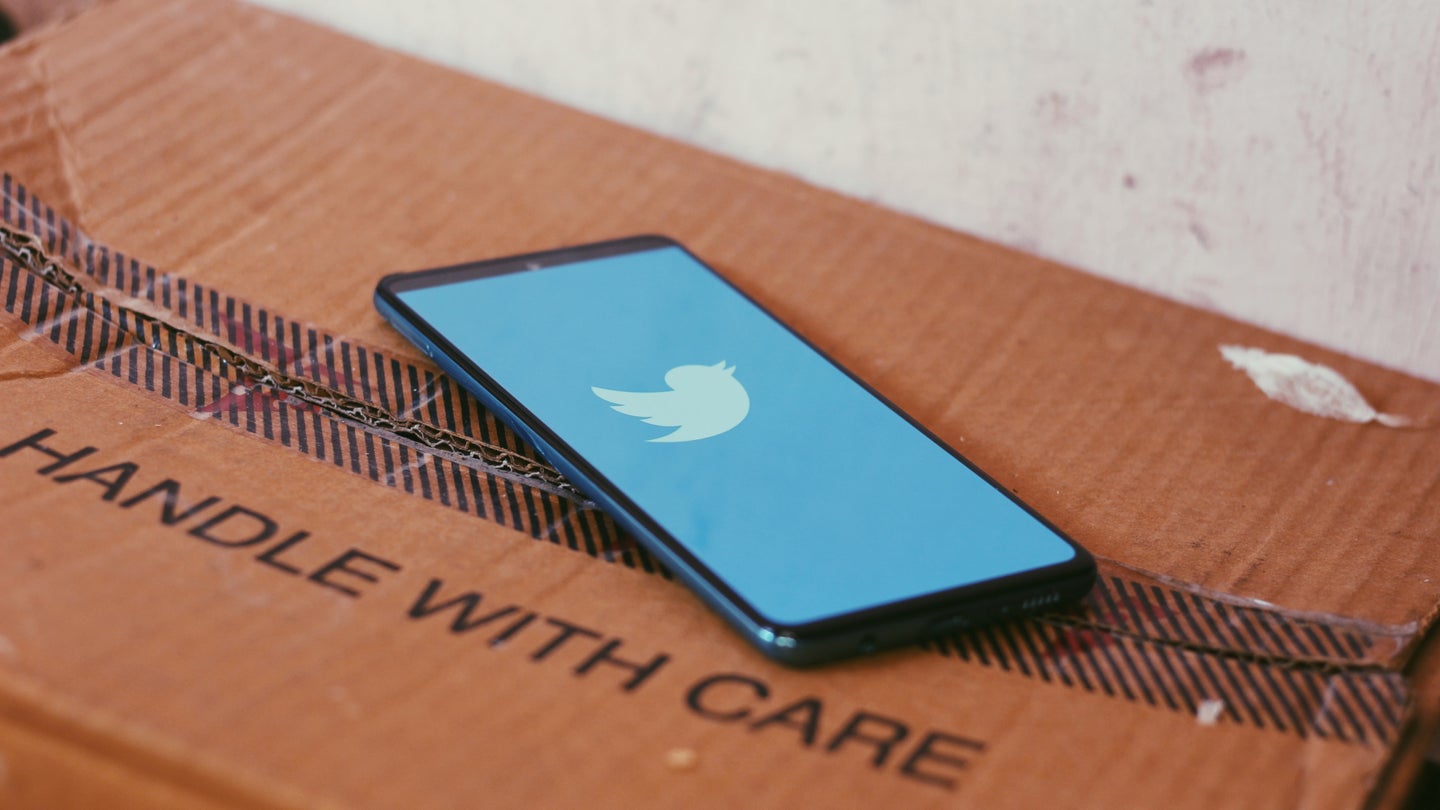 A phone with the Twitter icon on the screen, on top of a closed cardboard box that says "Handle with care."