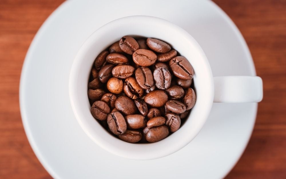 A white small coffee cup with coffee beans in brown color.