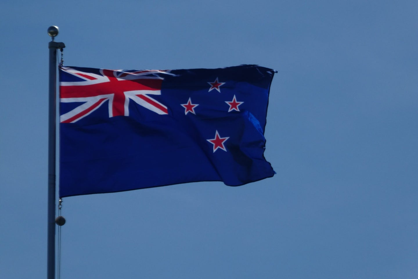 the new zealand flag on a flagpole against a blue sky