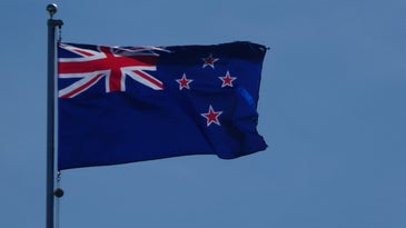 the new zealand flag on a flagpole against a blue sky