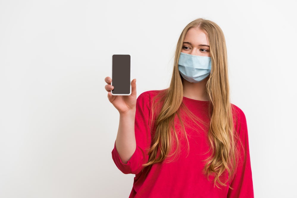 Someone holding a cellphone and wearing a mask