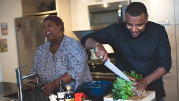 Black man and woman couple cooking with salad ingredients in kitchen