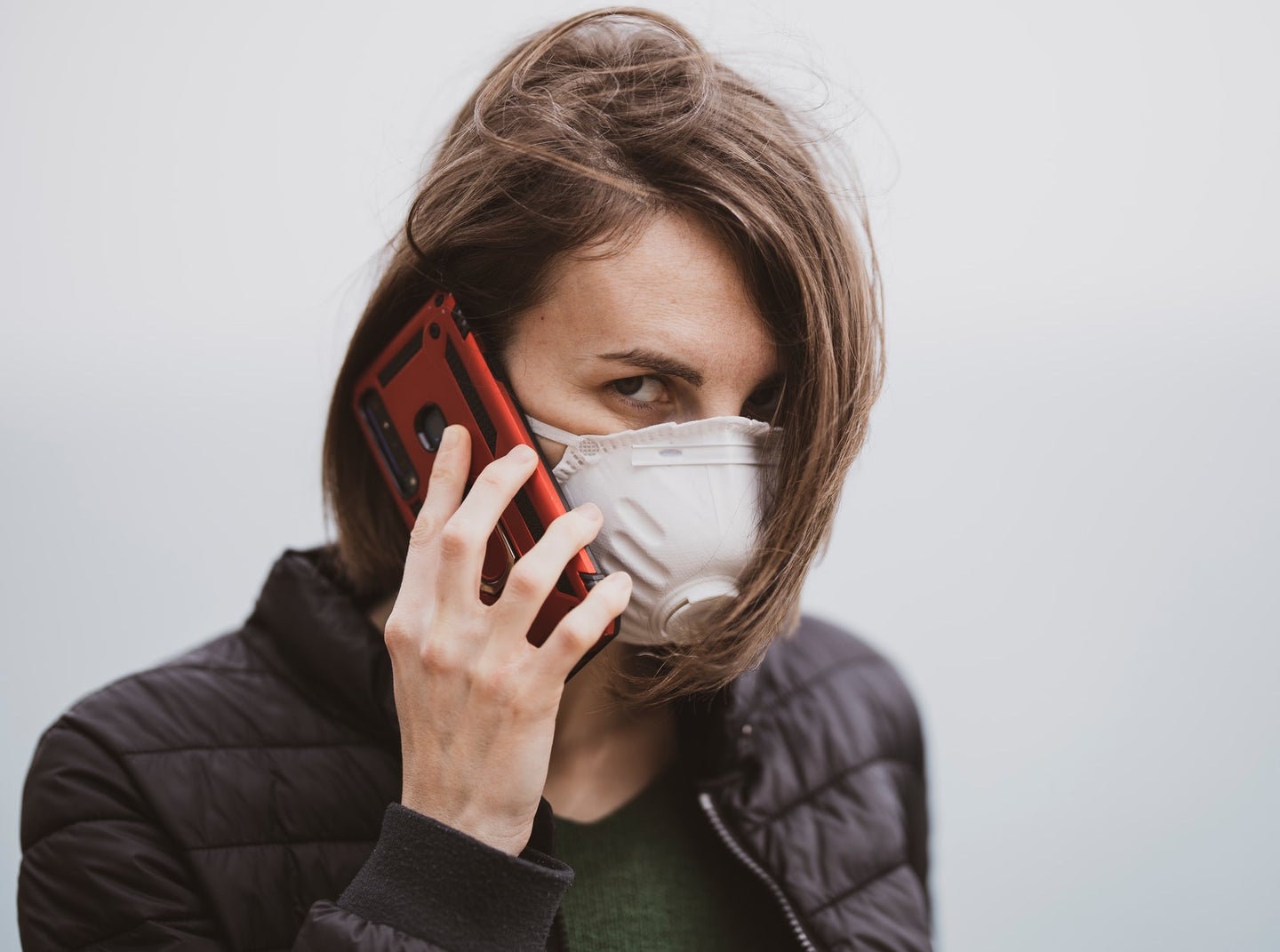 a woman is talking on the phone while wearing a protective face mask. The mask is white and has a plastic valve on the front of it.