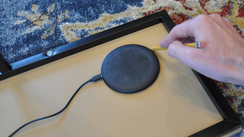 a person tracing a wireless charging pad on the bottom of an end table