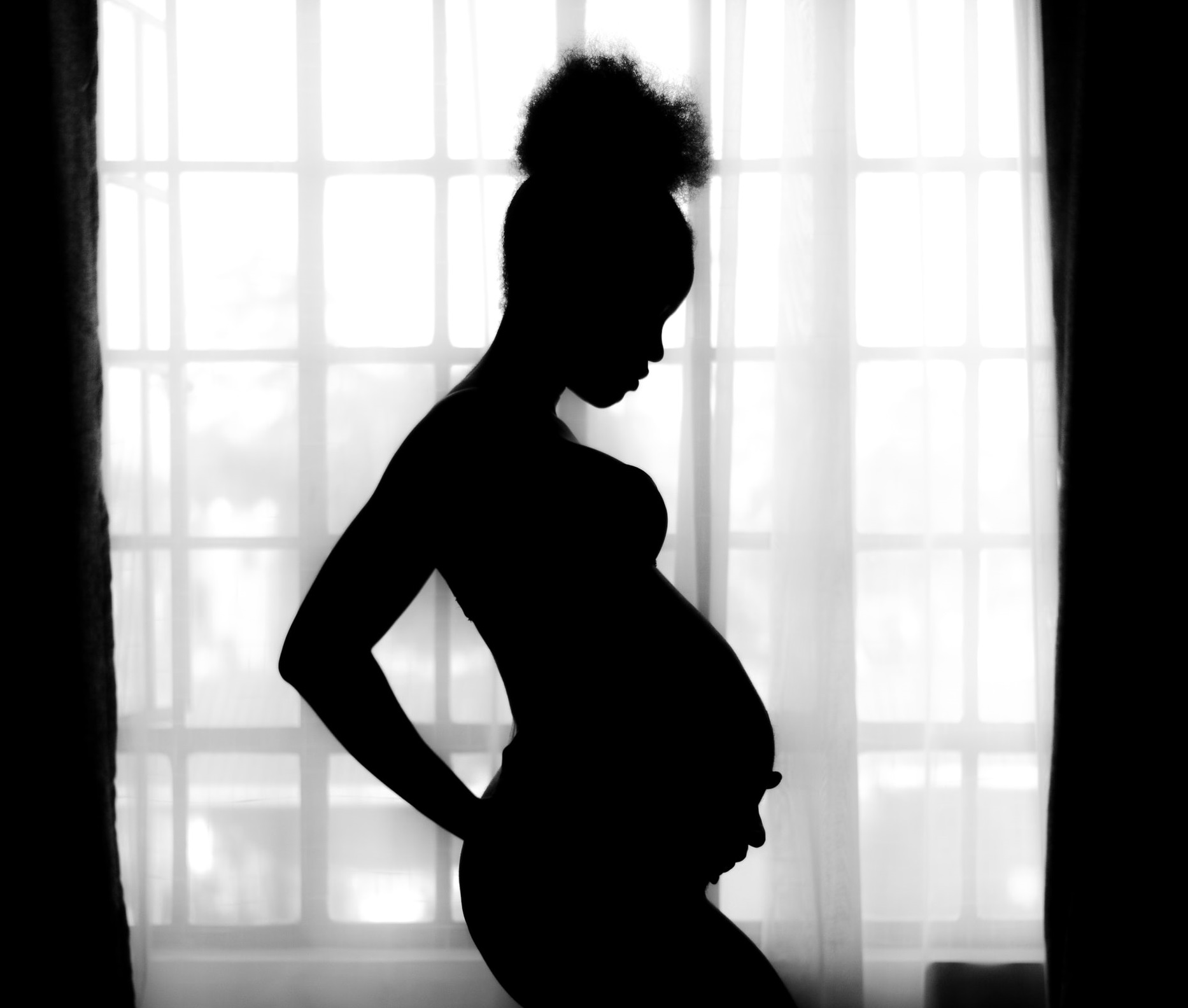 A Black pregnant person standing in silhouette