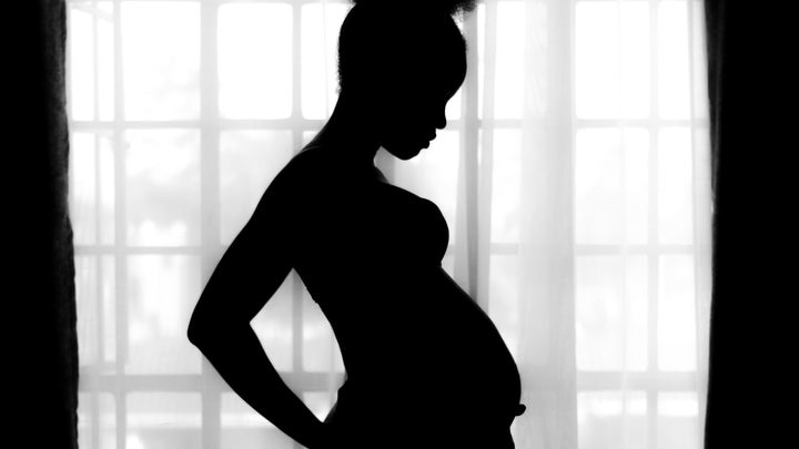A Black pregnant person standing in silhouette