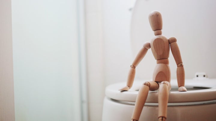 a wooden doll sitting on a toilet