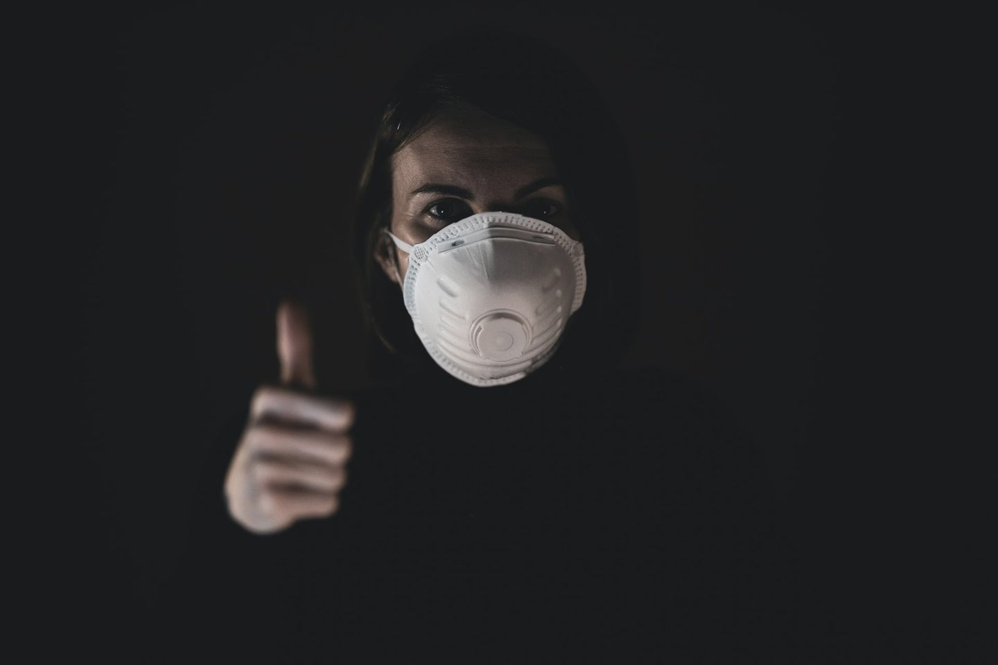 A person wearing an N95 mask and making a thumbs up
