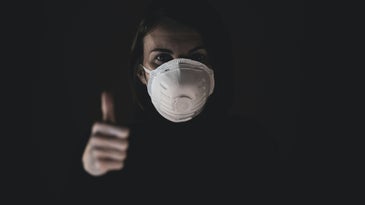 A person wearing an N95 mask and making a thumbs up