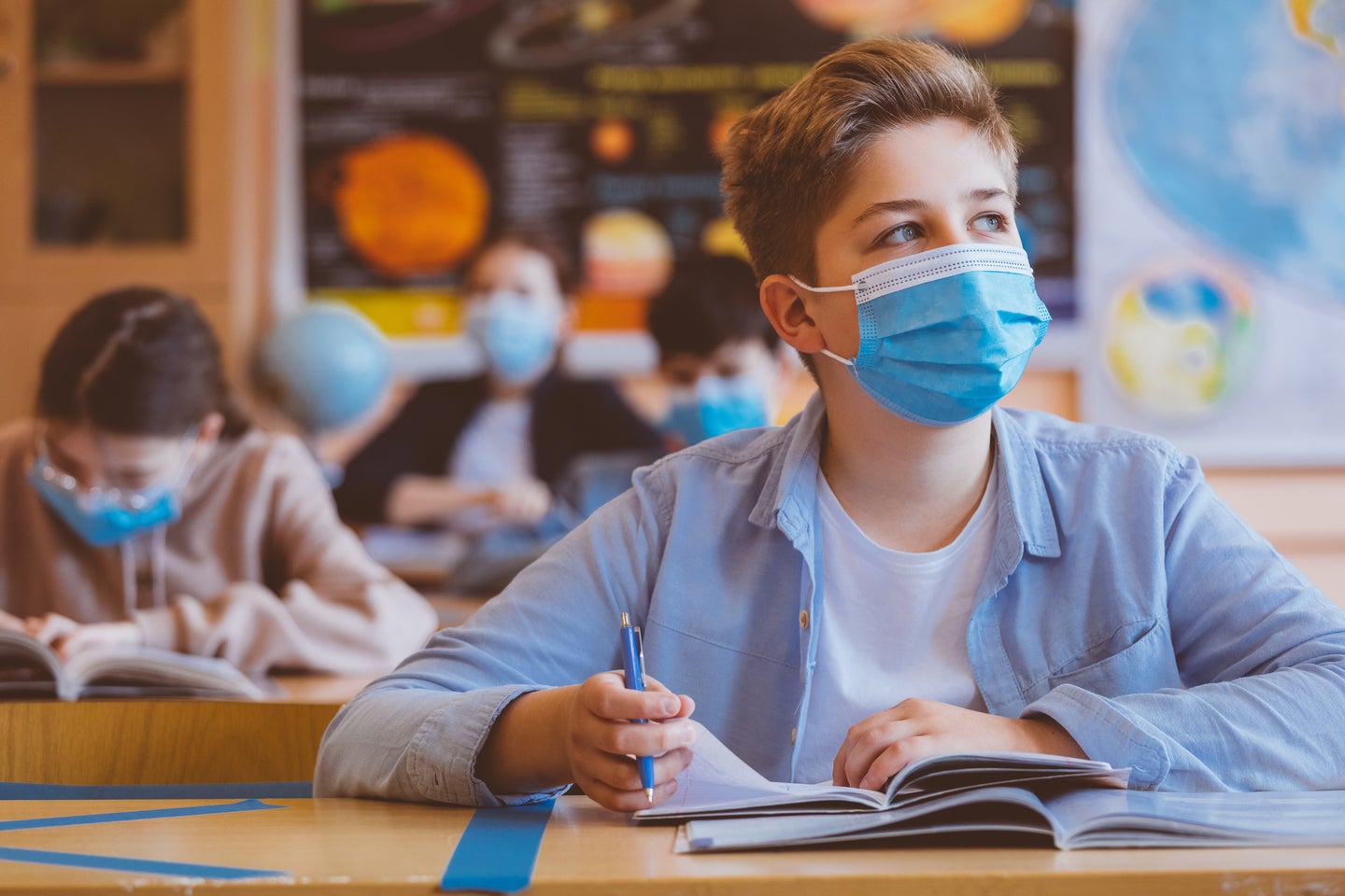 High school students at school, wearing N95 Face masks. Teenage boy sitting at the school desk, looking away and thinking.