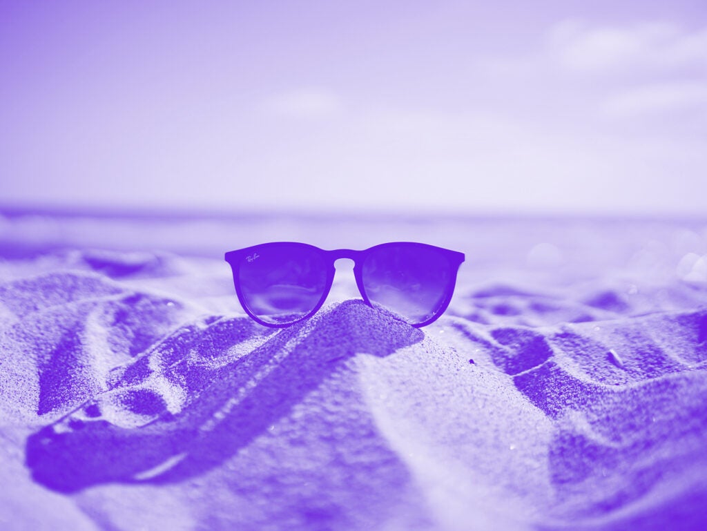 purple monochrome photo of sunglasses on sand