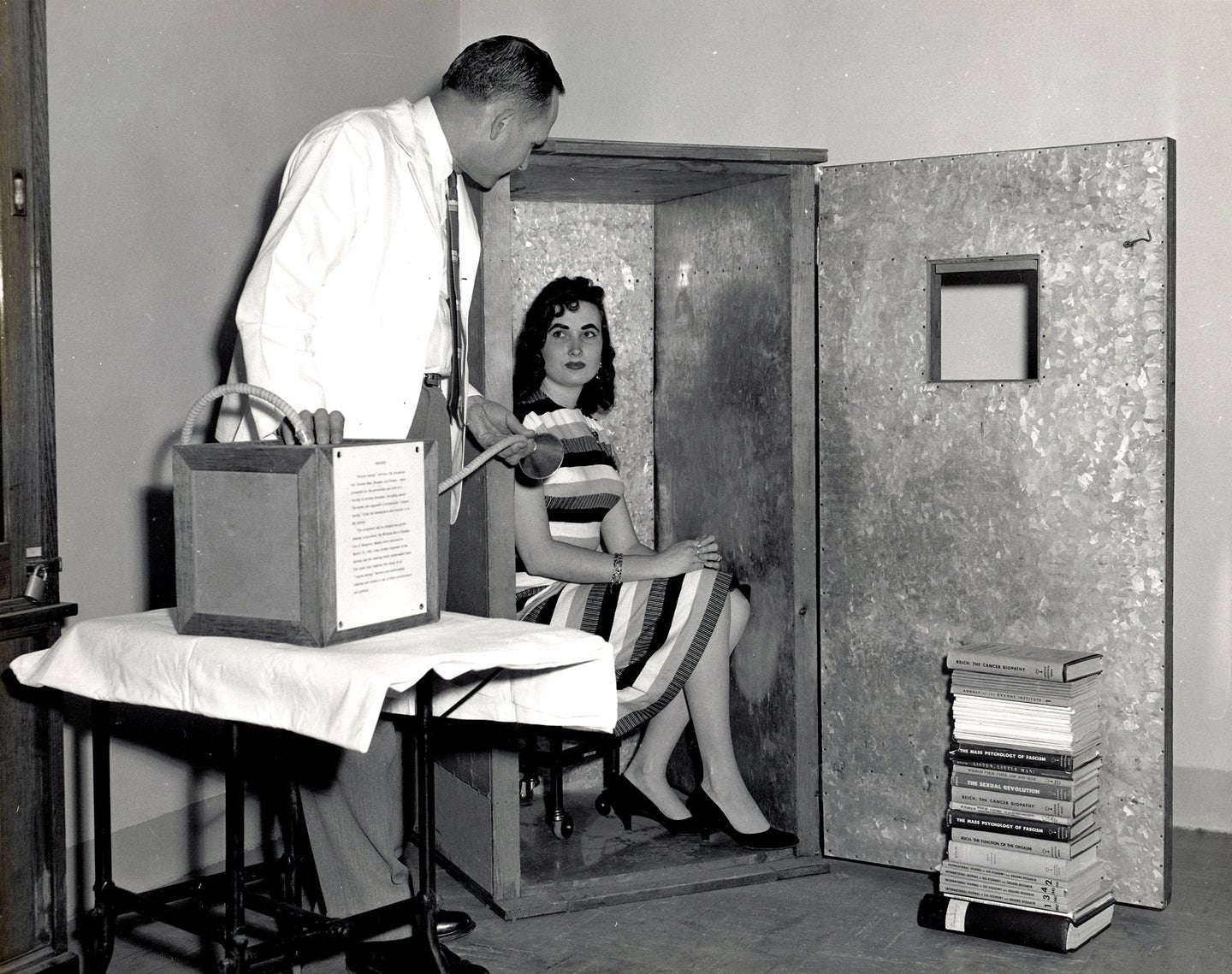a woman sits in a metal box while a man speaks to her