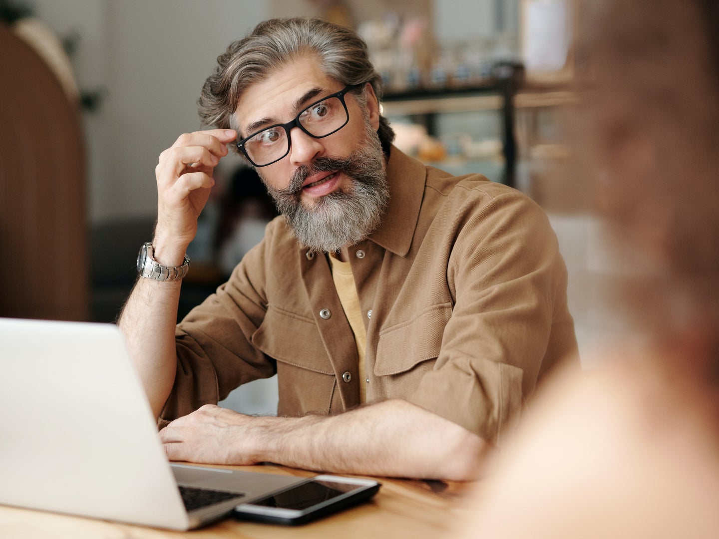 a bearded man with glasses looking stressed and confused while using a laptop computer