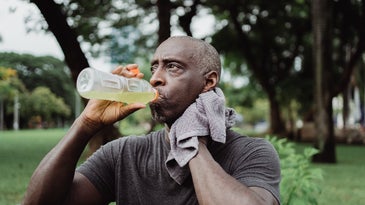 man drinking sports drink sweating sitting on bench