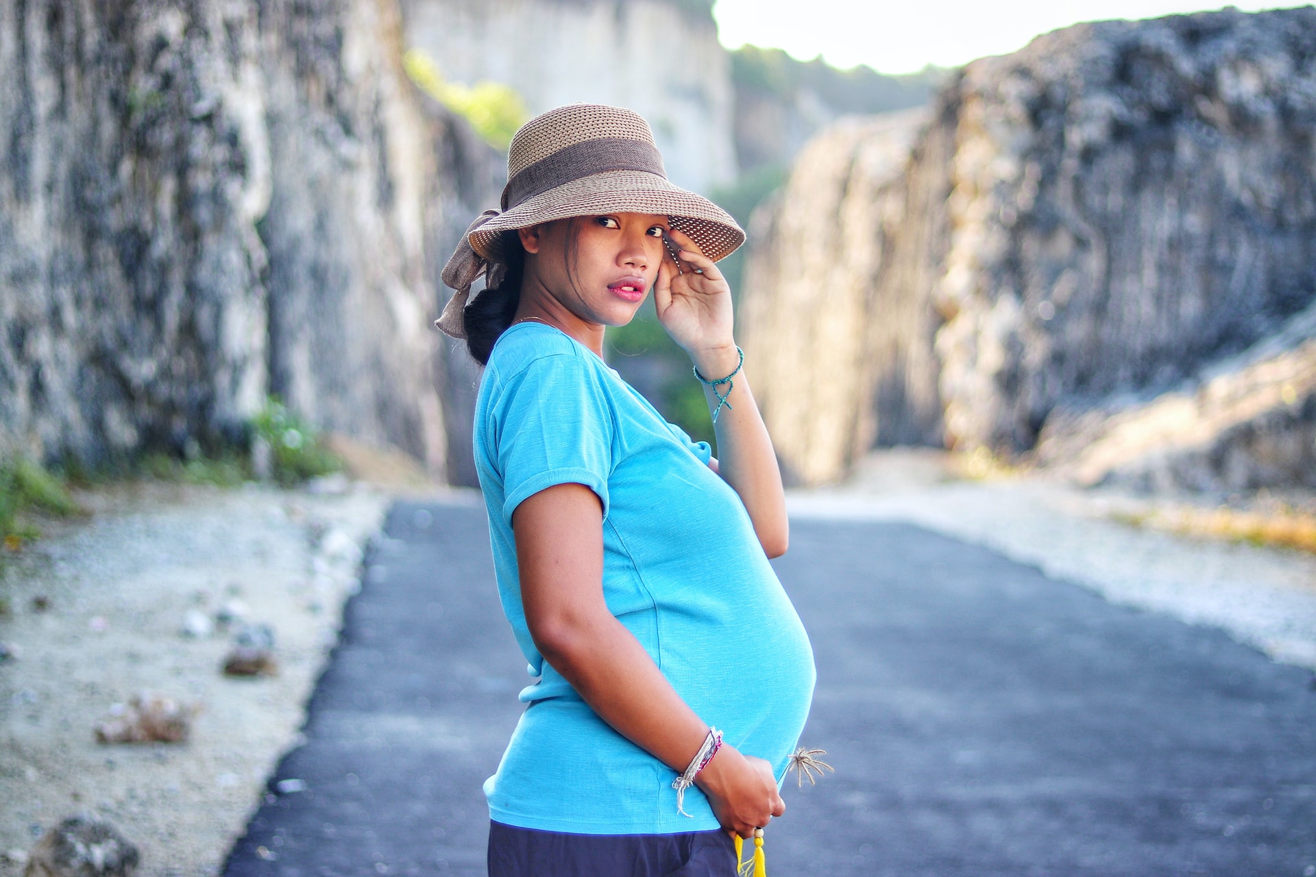 A pregnant person in a straw hat and blue shirt