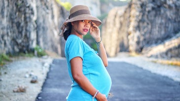 A pregnant person in a straw hat and blue shirt