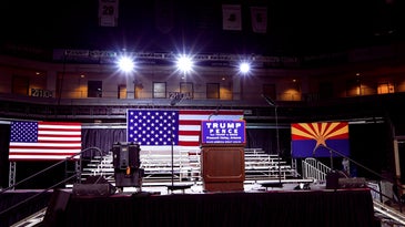 A stage with an American flag and a Trump campaign sign