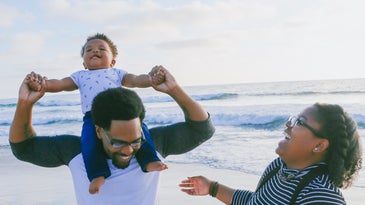 A Black family enjoying the beach with their toddler