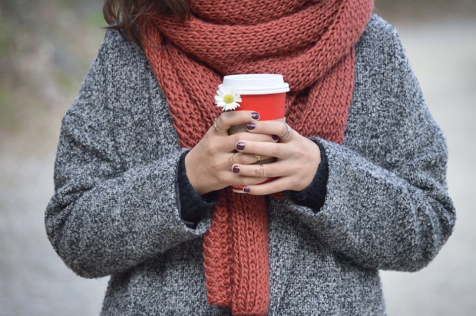 person wearing a scarf and holding a cup of coffee