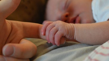 newborn baby holding mother's finger