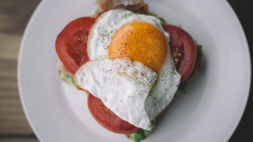 a fried egg on top of tomatoes on a white plate