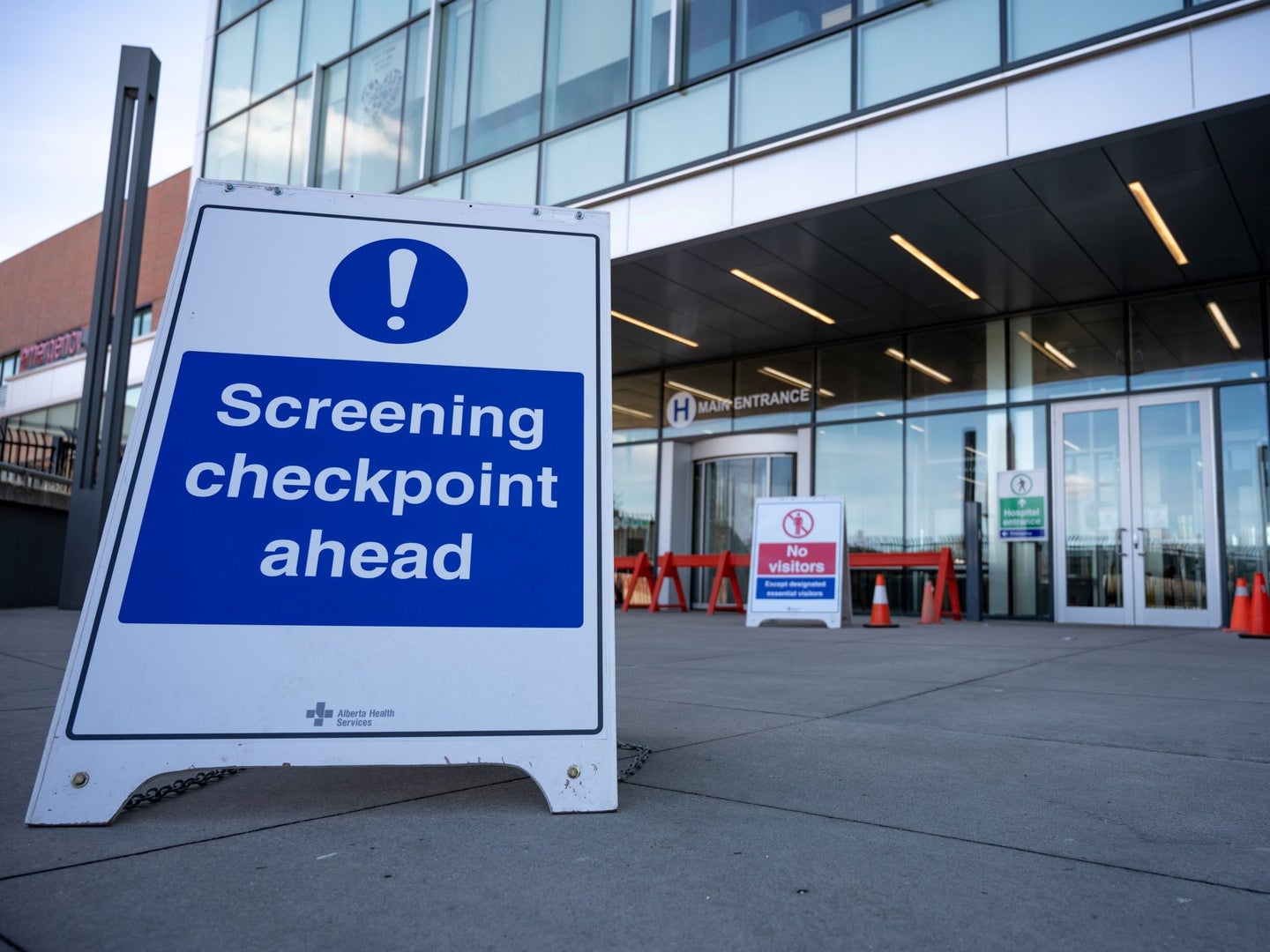 A sign that says "Screening checkpoint ahead" placed in front of the door to a hospital