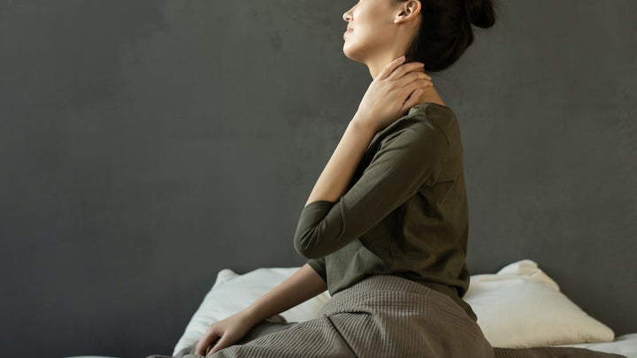 a woman sitting in bed with neck pain