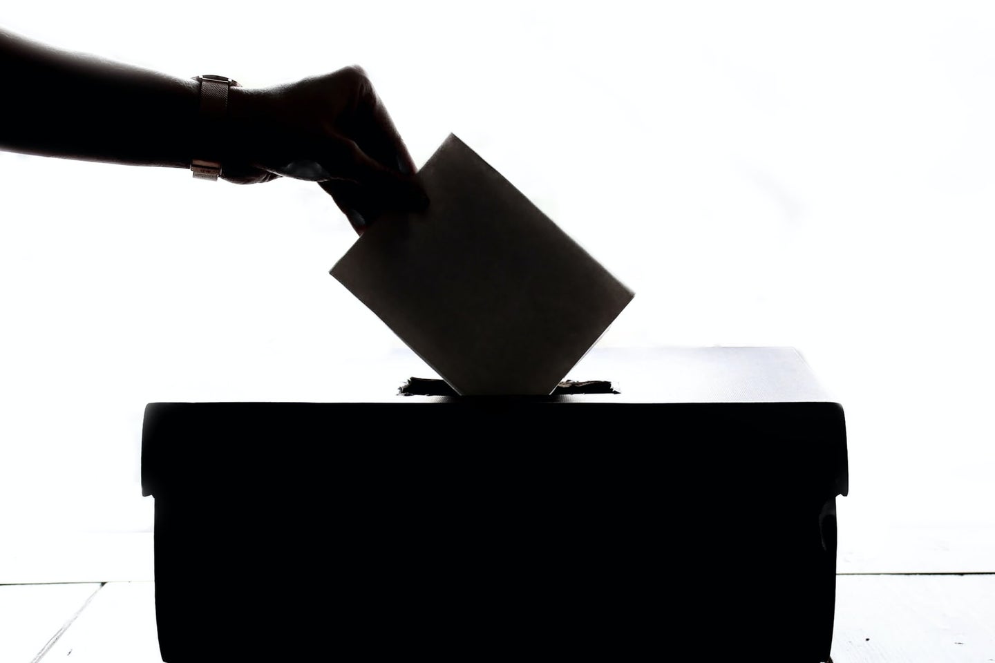 a hand putting a ballot into a box