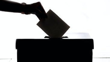 a hand putting a ballot into a box