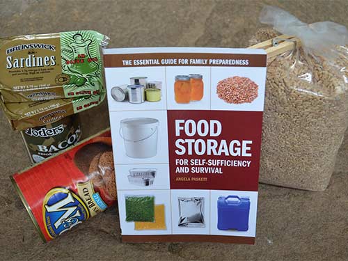 An assortment of supplies: Sardines, Beans, grains and a food storage book.