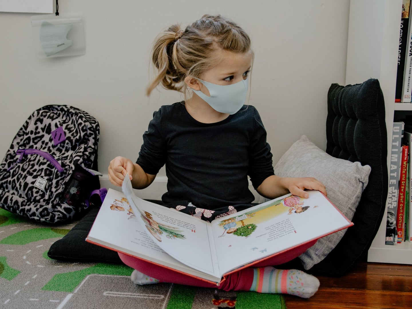 A child wearing a mask reading a picture book
