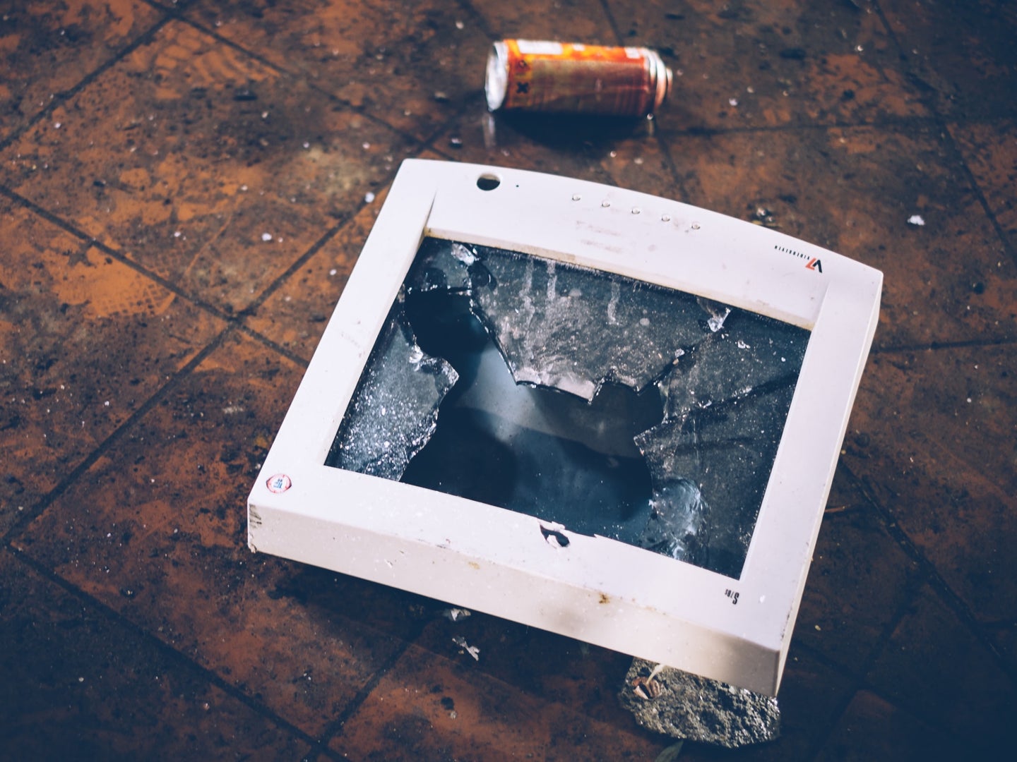 A smashed computer monitor on a floor near a discarded can—physical destruction is one way to permanently delete files.