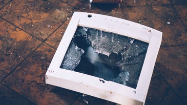 a smashed computer monitor on a floor near a discarded can