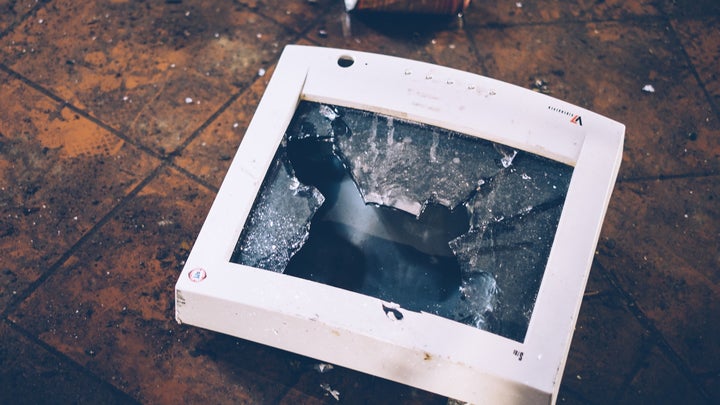 a smashed computer monitor on a floor near a discarded can
