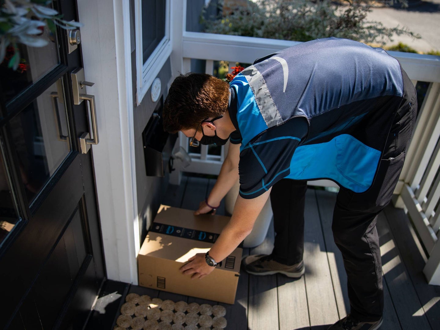 An Amazon delivery man putting an Amazon package on a porch in front of a door during the daytime.