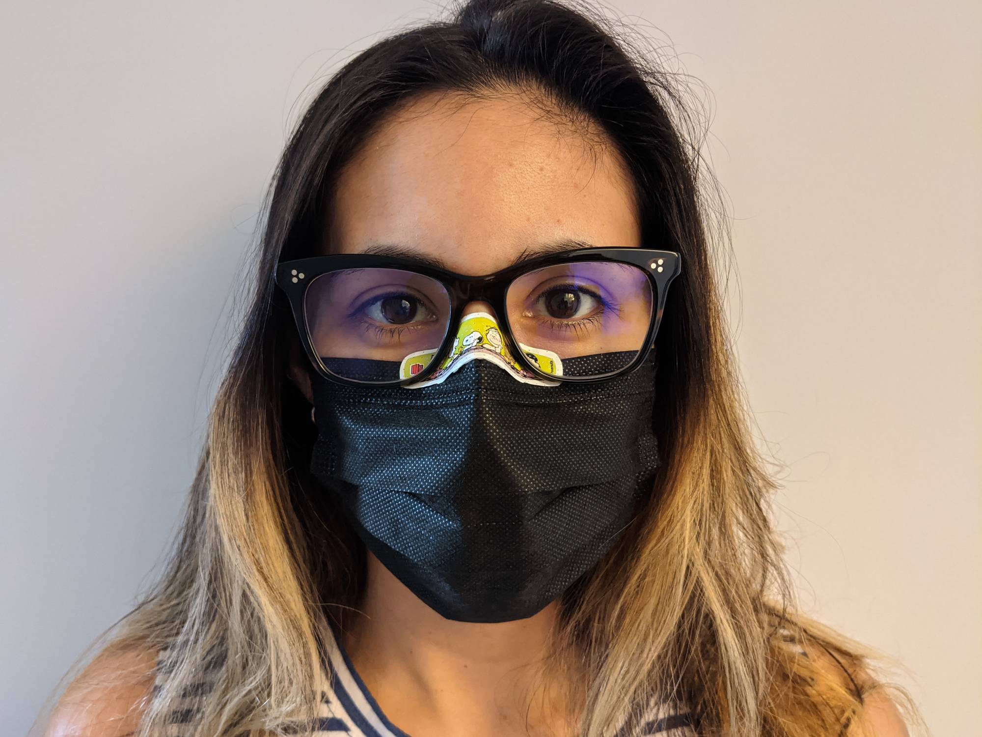 A blonde woman wearing a black face mask and glasses after she taped the mask to her nose to prevent lens fogging.