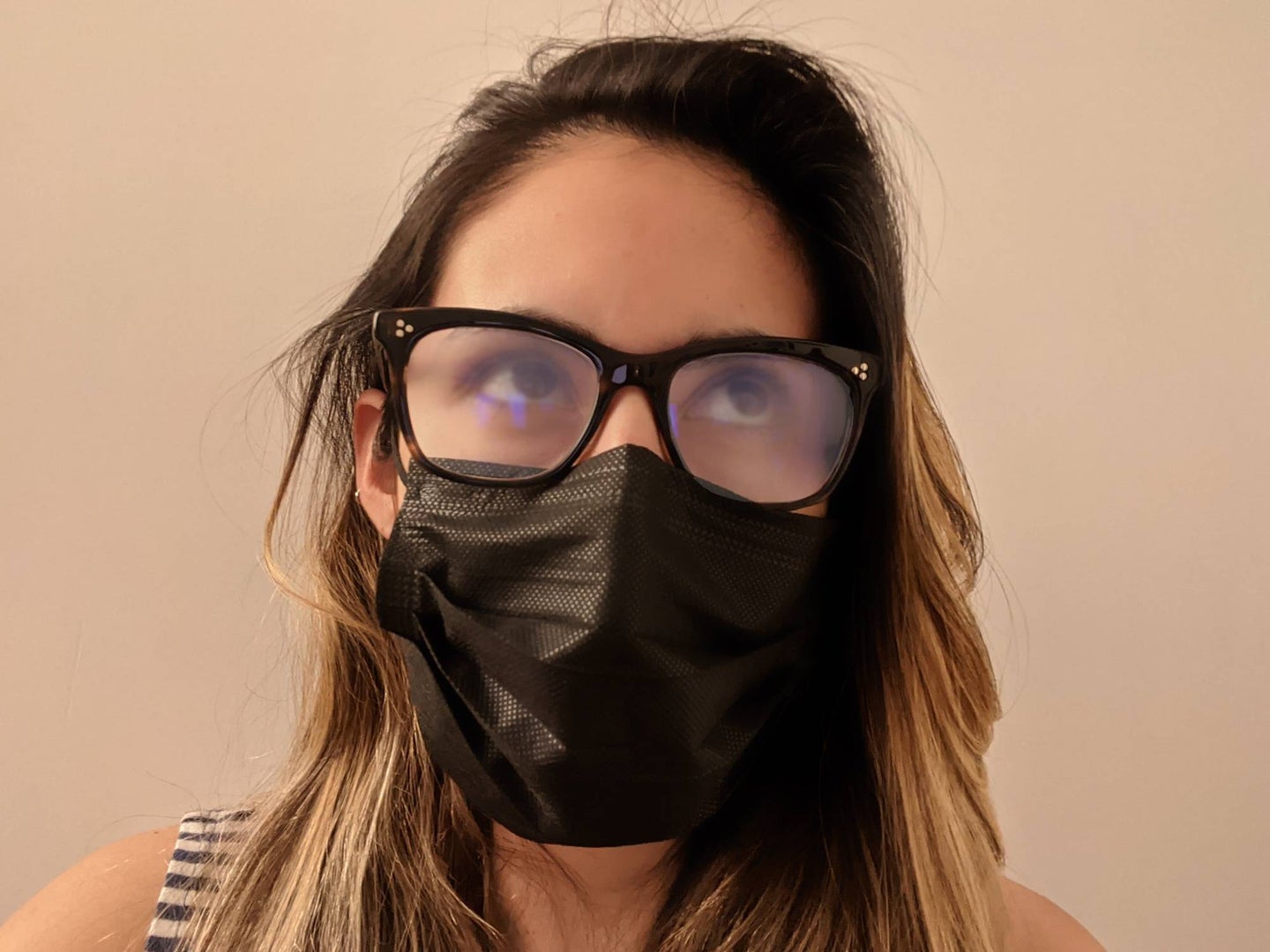 A frustrated blonde woman with fogged glasses while wearing a black face mask.