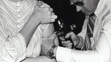 Black and white photo of a patient getting a swine flu vaccine through a jet injector in 1976