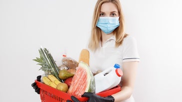 Person in a mask and disposable gloves holding a basket of groceries