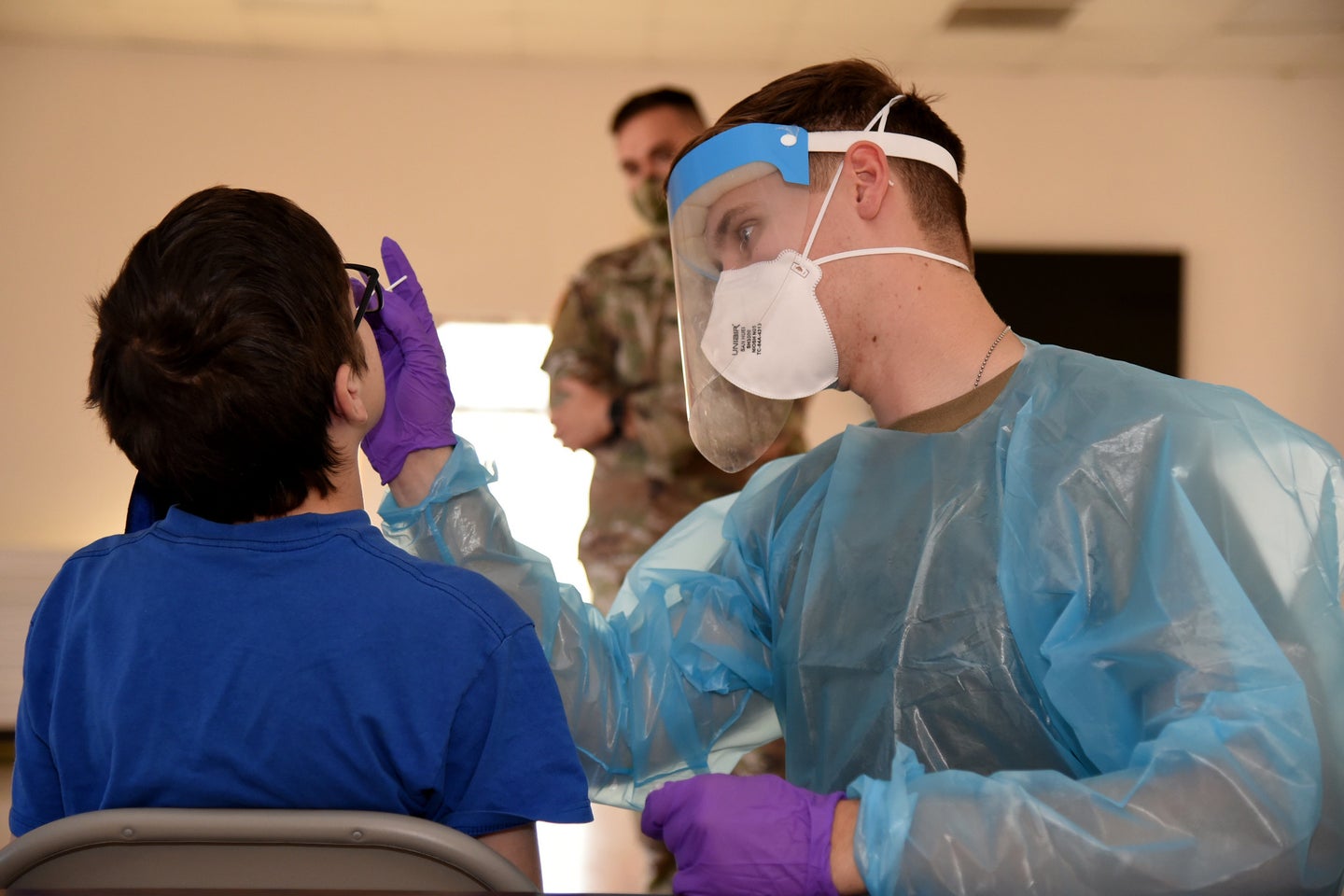 A kid gets a traditional nasal-swab test from a doctor in PPE