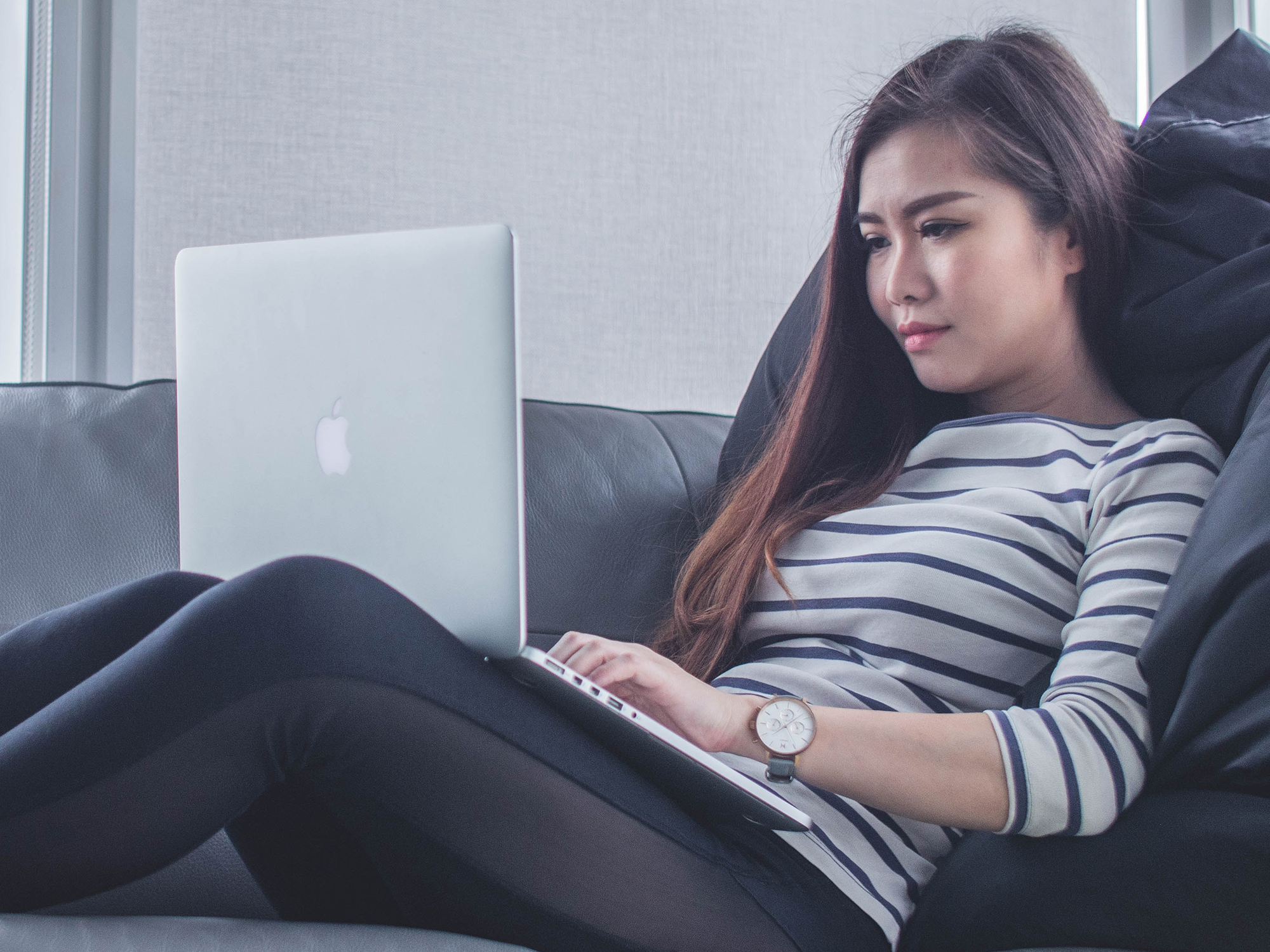A woman lounging on a couch with a silver Macbook on her lap, possibly considering how she can create shortcuts for macOS.