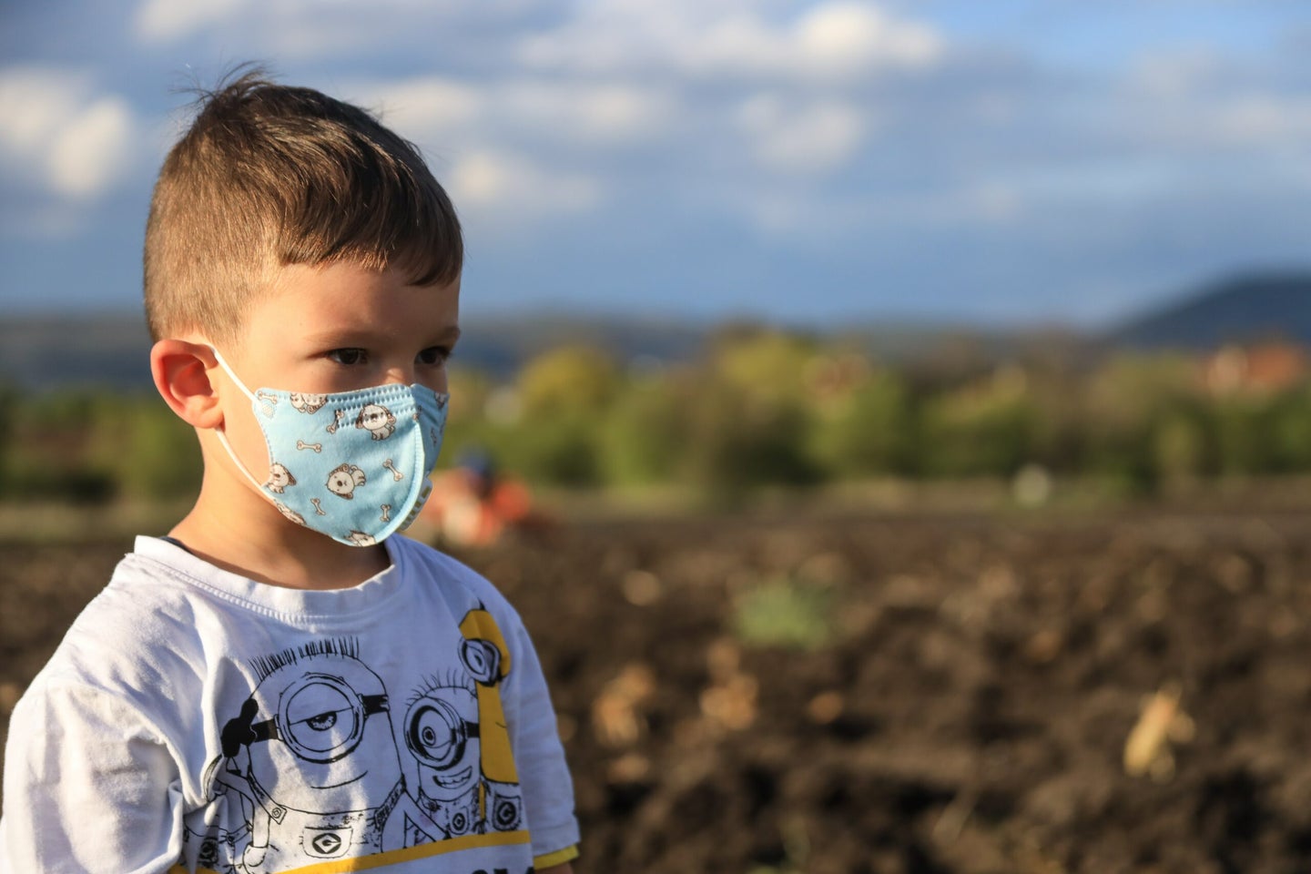 A kid with a cartoon-themed mask standing in a field