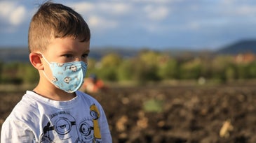 A kid with a cartoon-themed mask standing in a field