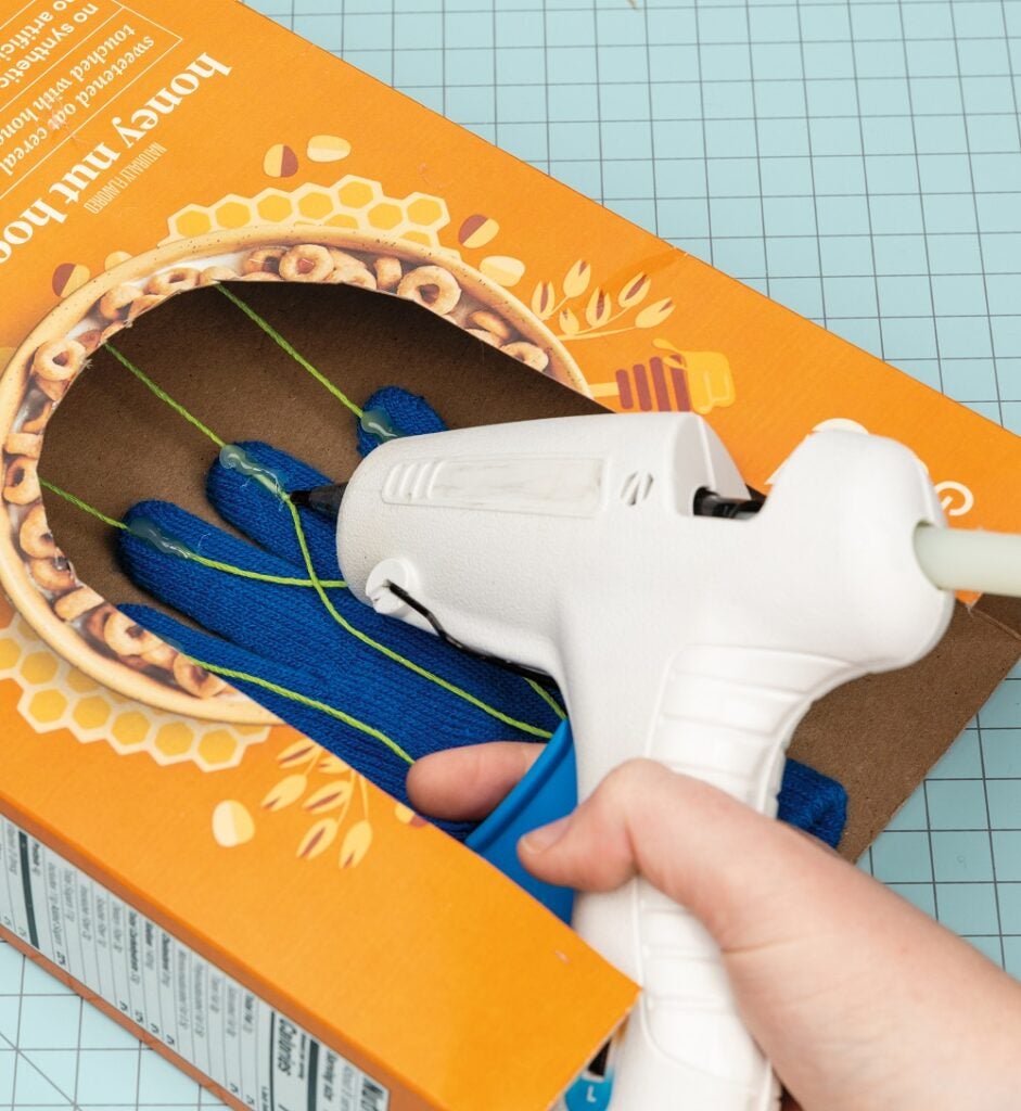 Gluing the strings onto the glove in the cereal box
