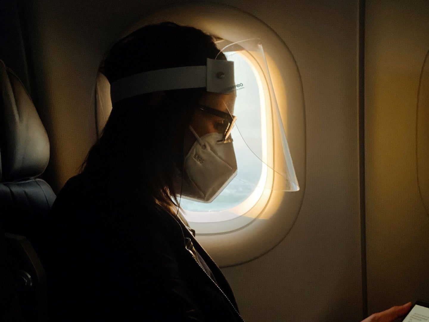 A woman wearing a face mask and face shield on an airplane