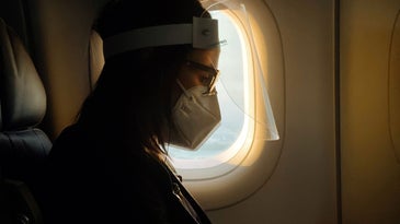 A woman wearing a face mask and face shield on an airplane